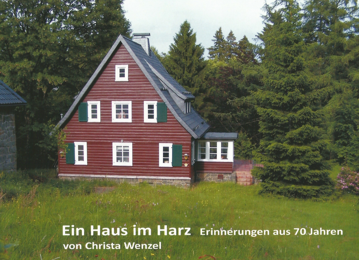 Ein typisches Hahnenkleer Haus aus den 1930er Jahren mit Holzbeschlag und Grauwackefundament steht auf einer blühenden Bergwiese.