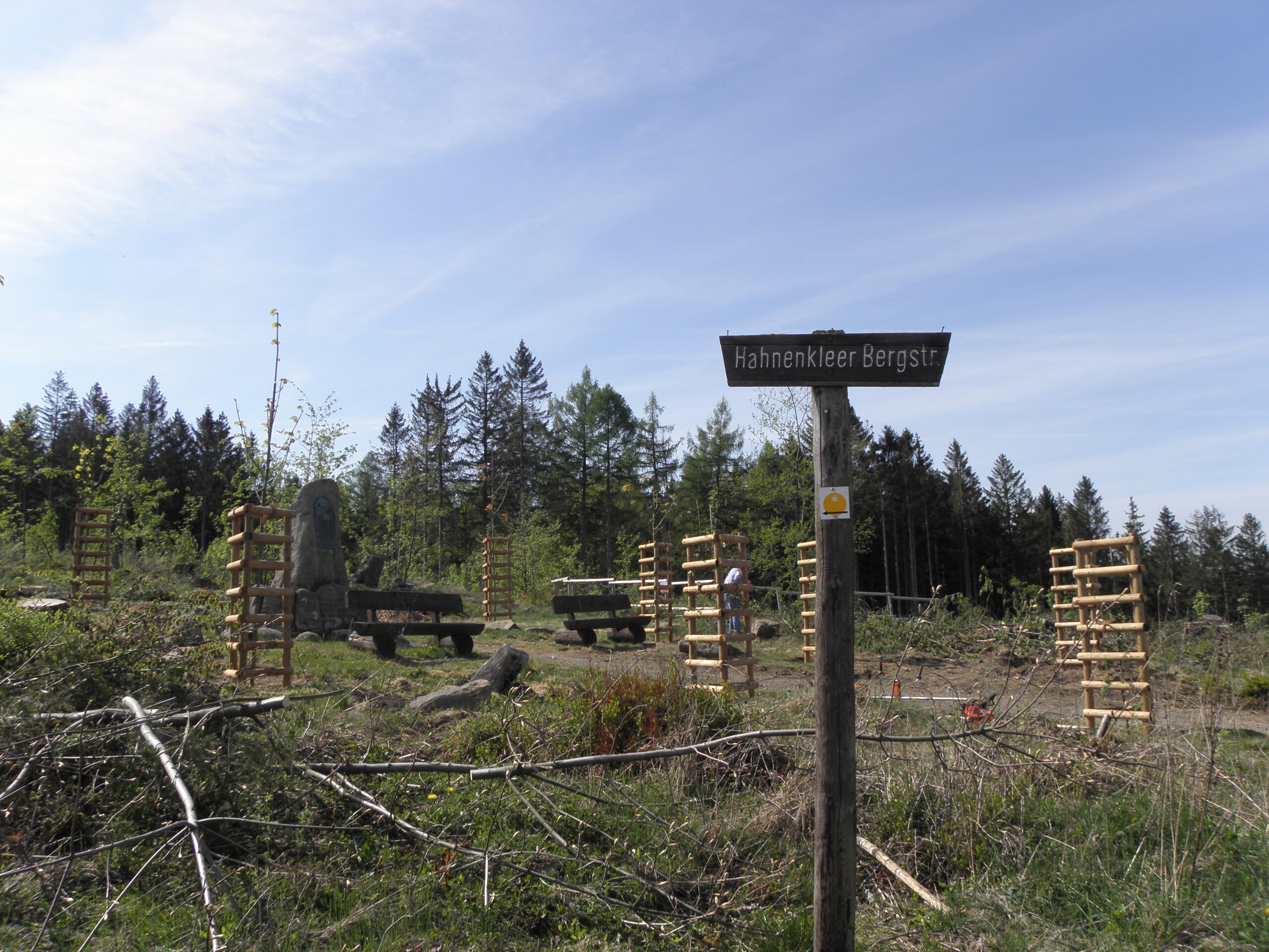 Um ein großes Granitdenkmal herum befinden sich frisch gepflanzte Laubbäume, die von Holzgattern umgeben gegen Wildverbiss geschützt sind